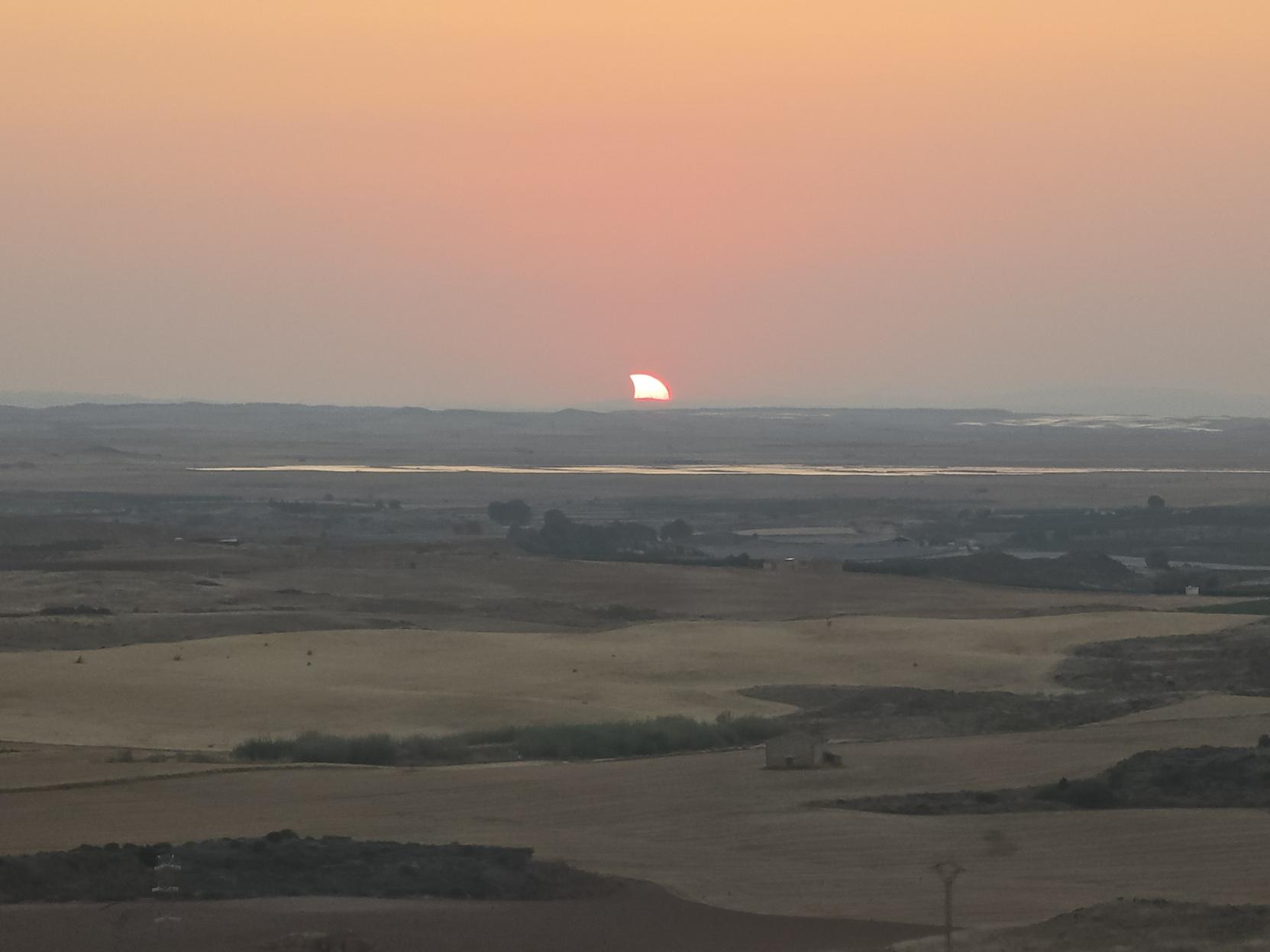 one last photo of the eclipsed sunset, the eclipsed sun is halfway above the horizon, looking like a shark fin